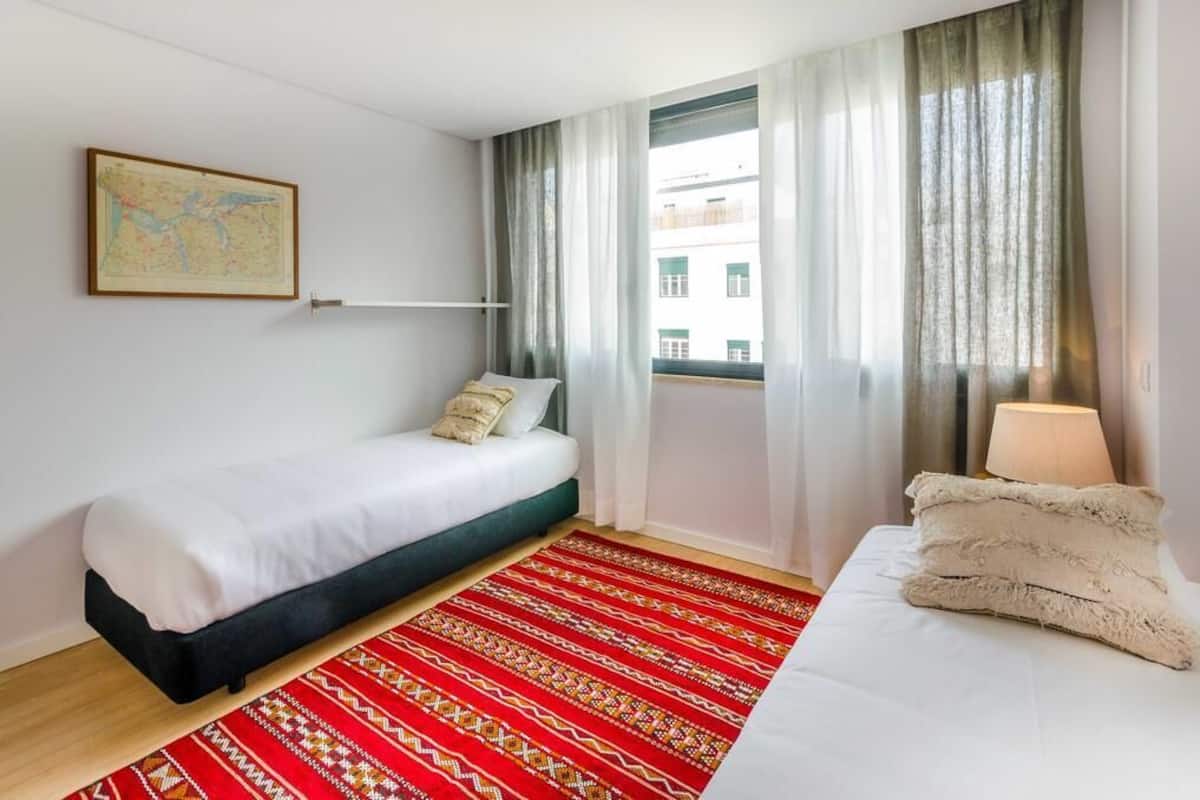 A hotel room with a bed, a red patterned rug, a map on the wall, and a window with curtains.