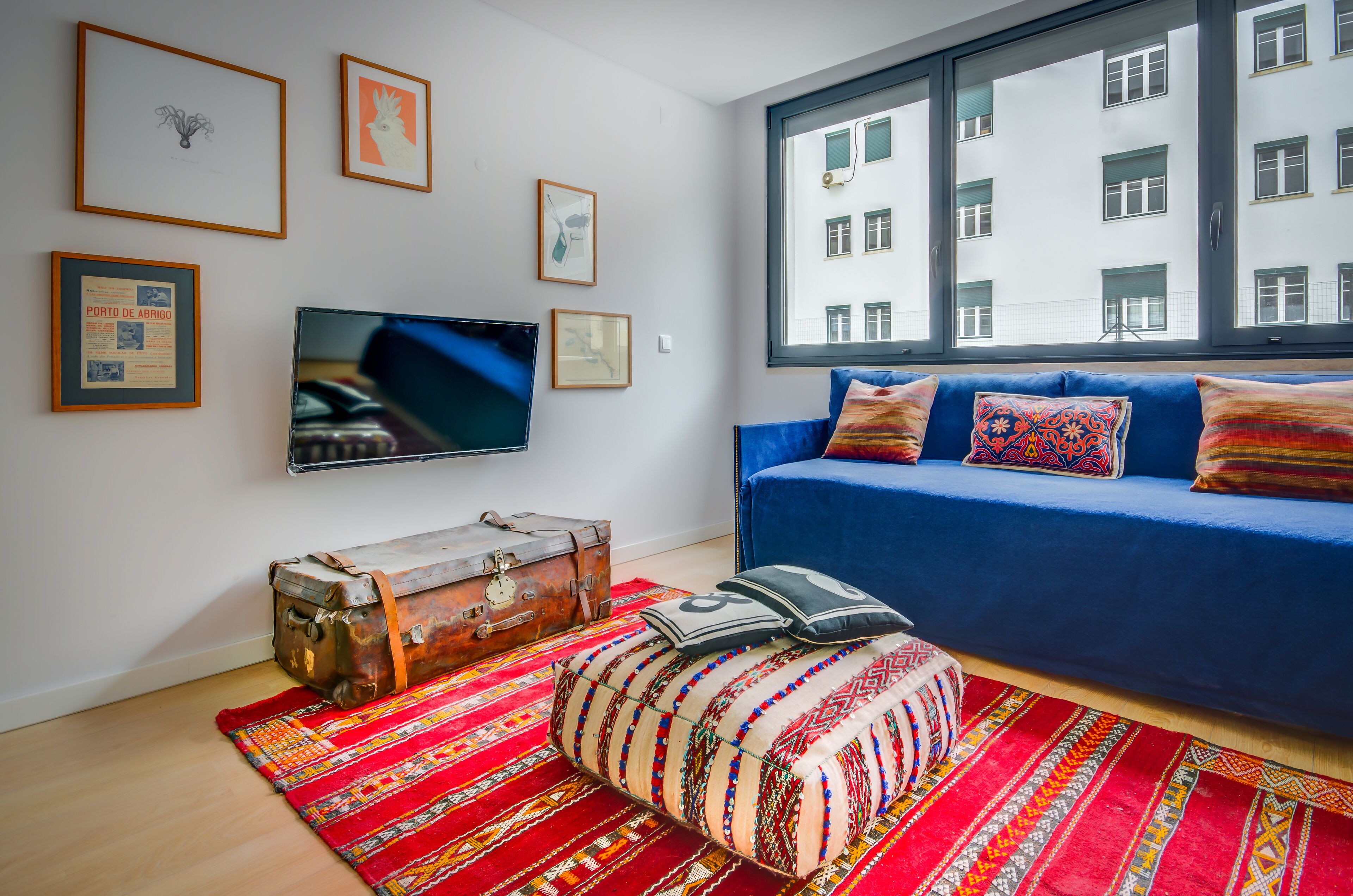 A room with a blue sofa, a television, a suitcase, and a colorful rug.