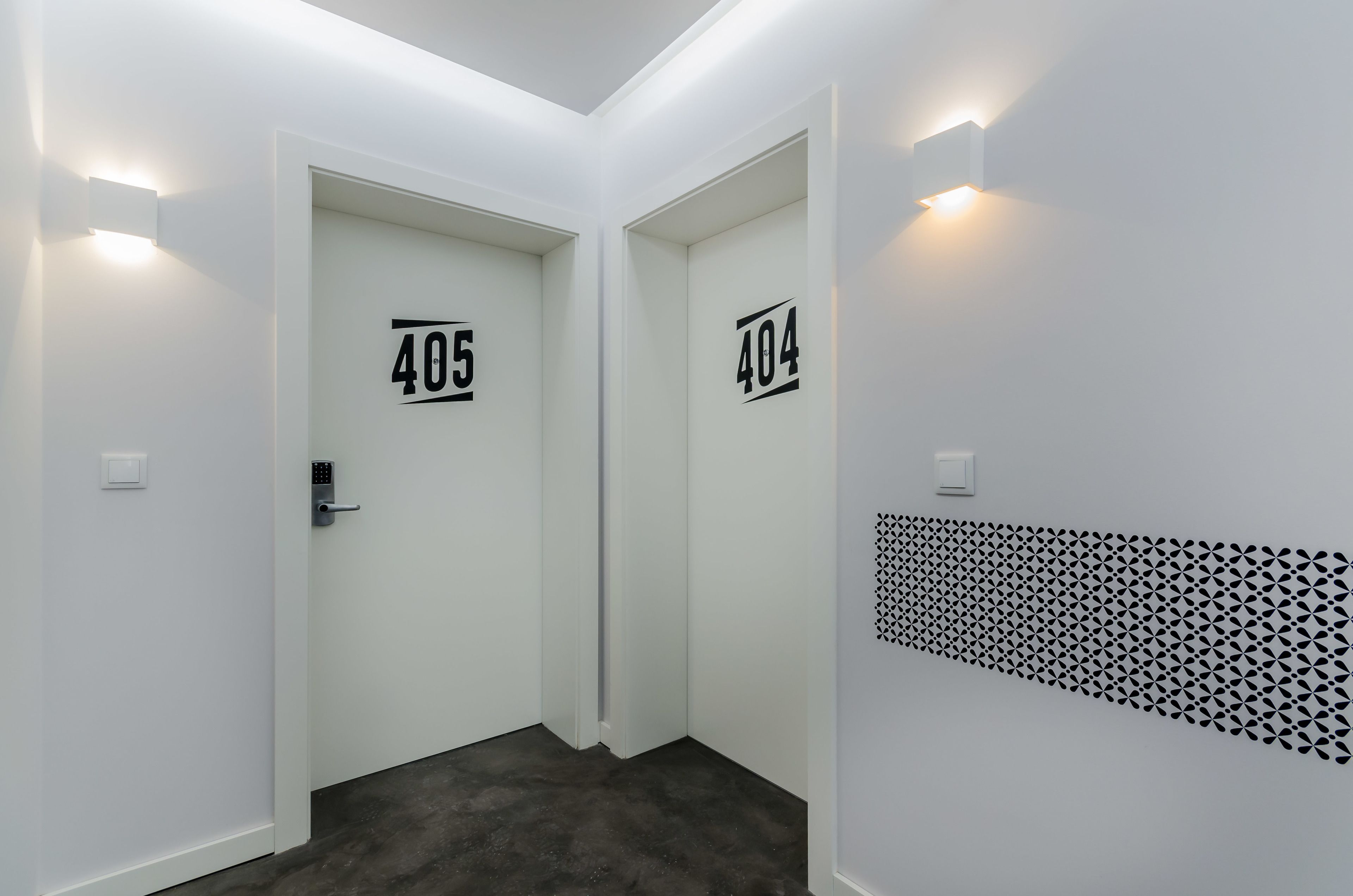 Un pasillo con puertas que indican los números 405 y 404, un revestimiento de pared estampado y una lámpara.