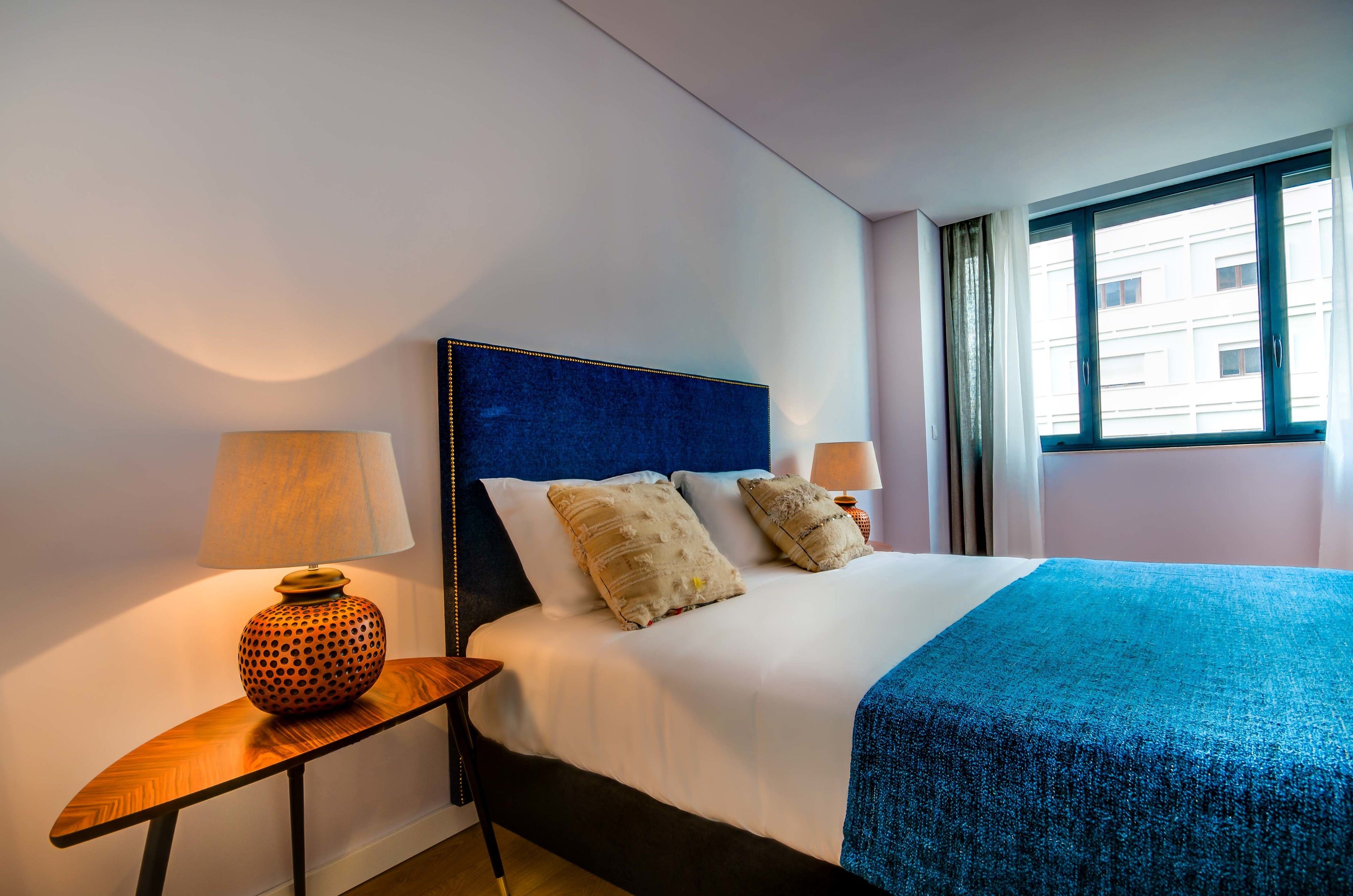 A hotel room with a large bed, two bedside lamps, and a window with curtains.