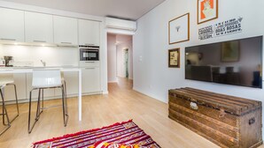 A modern kitchen with white cabinets, a built-in oven, and a dining area with two bar stools. - LSA Liberdade by Numa (Lisbon)