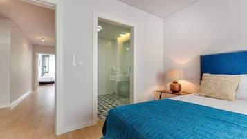 A bedroom with a bed, a nightstand with a lamp, and a bathroom visible through an open door.