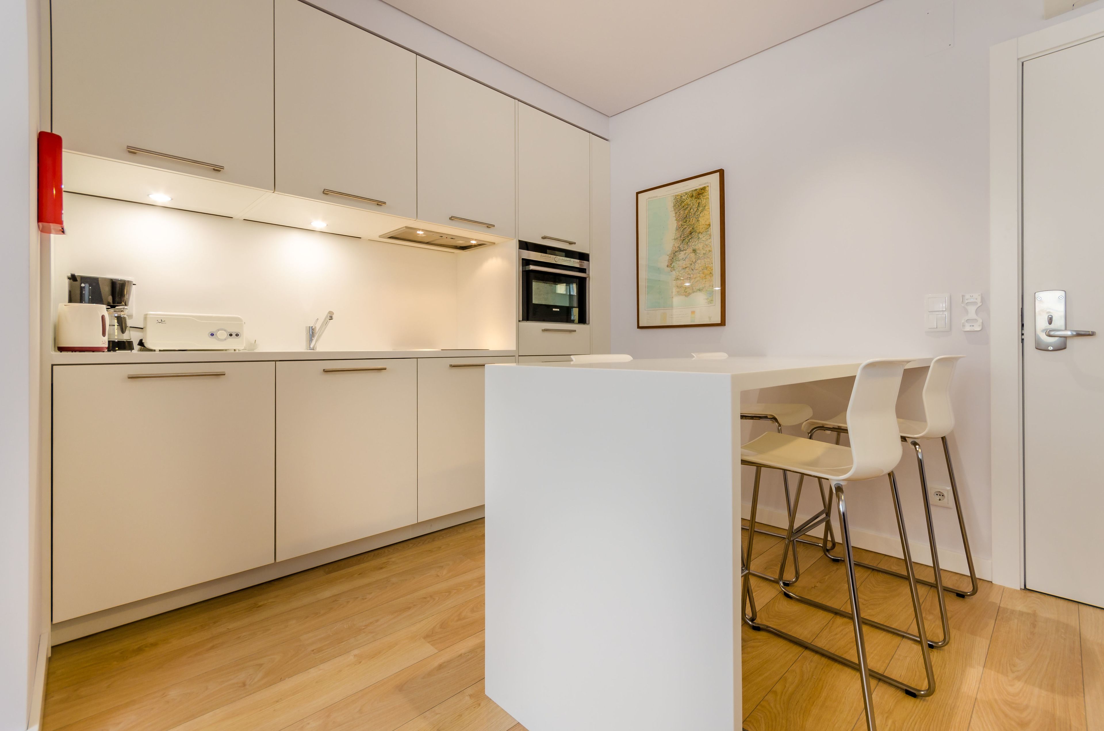 Una cocina moderna con armarios blancos, una cafetera y un comedor con sillas blancas.