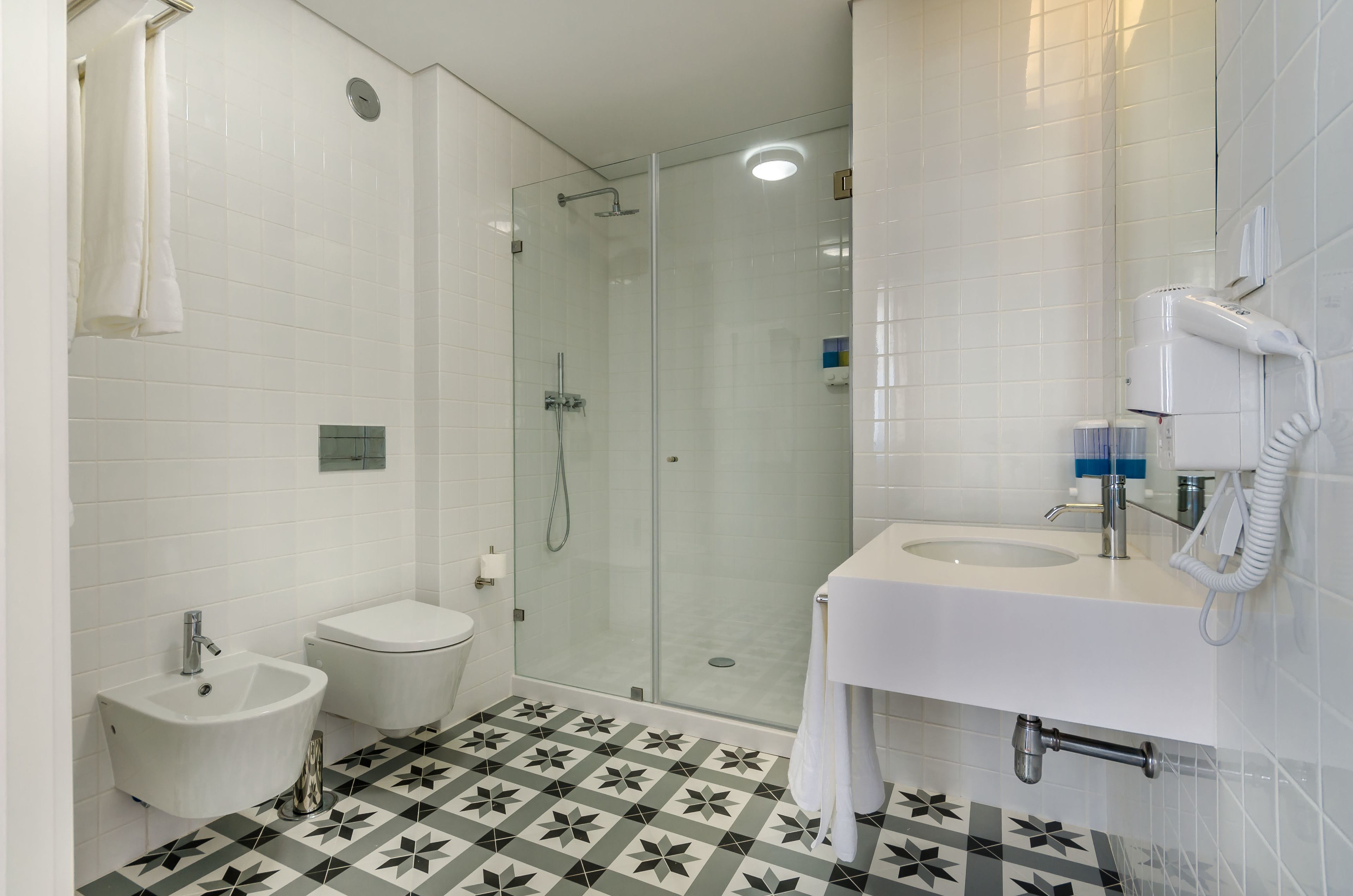 A bathroom with a glass-enclosed shower, a bidet, a toilet, and a sink with a towel rack.