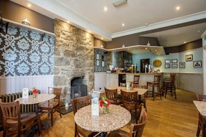 A restaurant with round tables and chairs, a stone wall, and a bar area. - Inn At The Park (Aberdeen)