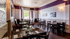 A dining area with multiple tables and chairs, a large window with curtains, and patterned wallpaper. - Inn At The Park (Aberdeen)