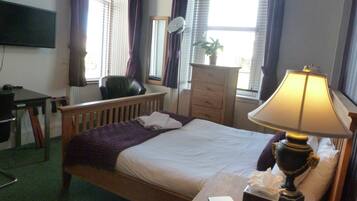 A hotel room with a bed, a desk, a chair, a dresser, a lamp, and a TV on the wall.