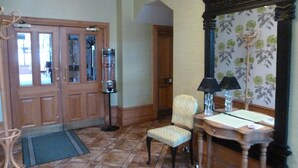 A room with a wooden door, a mirror, a chair, a desk, and a floor lamp. - Inn At The Park (Aberdeen)