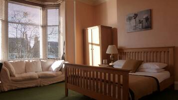 A bedroom with a bed, a wooden headboard, a nightstand, a lamp, a wardrobe, and a window with blinds.