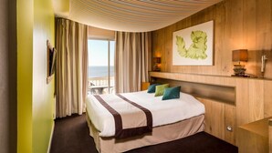 A hotel room with a bed, a view of the sea, a painting on the wall, and a wooden headboard. - Le Calluna (Prefailles)
