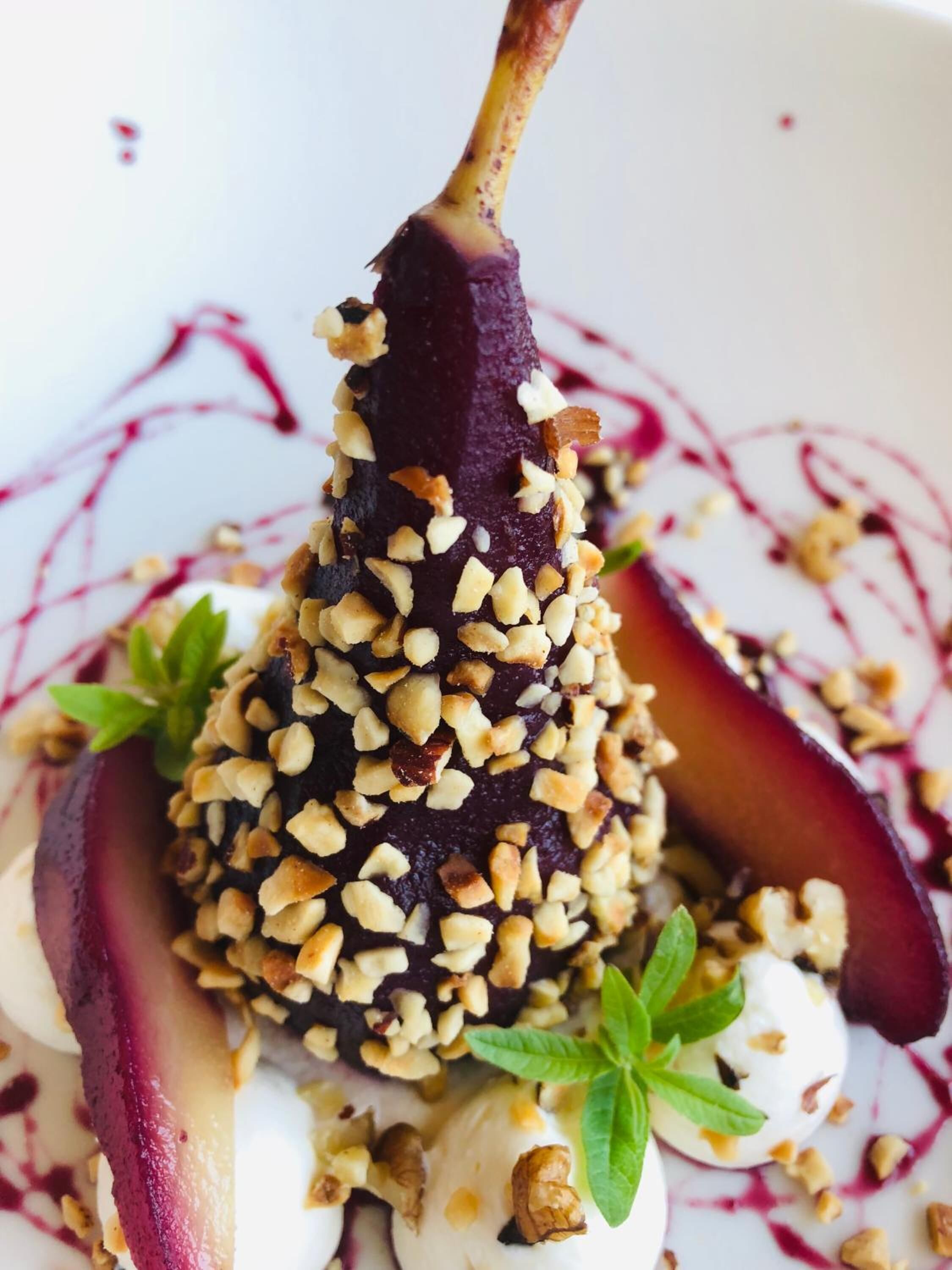 Ein Dessert mit dunkler Frucht, Nüssen und einem weißen, cremigen Belag, verziert mit grünen Blättern.