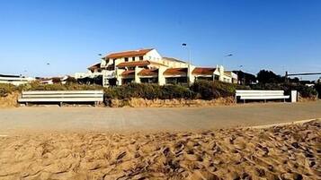 Un edificio sul lungomare con diversi balconi, una spiaggia sabbiosa in primo piano e un cielo azzurro.