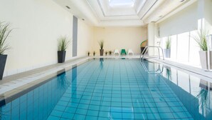An indoor swimming pool with a skylight, tiled floor, and potted plants. - Le Calluna (Prefailles)
