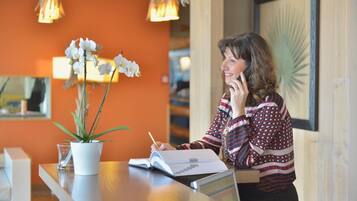 Une personne est assise à une table, devant un carnet, une plante en pot et un tableau encadré accroché au mur.