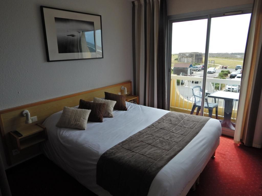 Habitación de hotel con una cama grande, una mesita de noche, una lámpara y vistas al exterior.