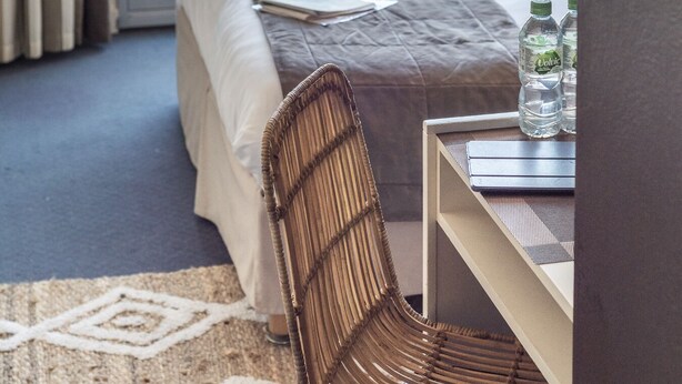A hotel room with a bed, a chair, a table with water bottles, and a view of the sea with boats. - Le Calluna (Prefailles)