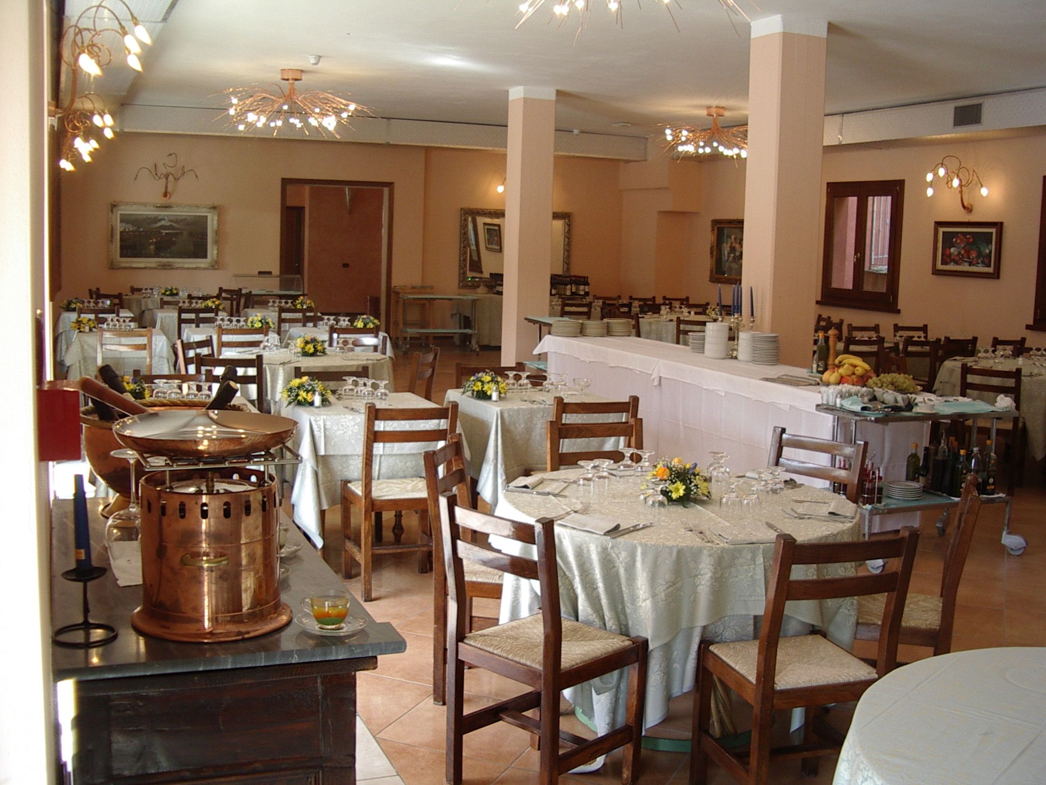 A restaurant with multiple dining tables set for guests, featuring a central bar area with a variety of food and drink items.