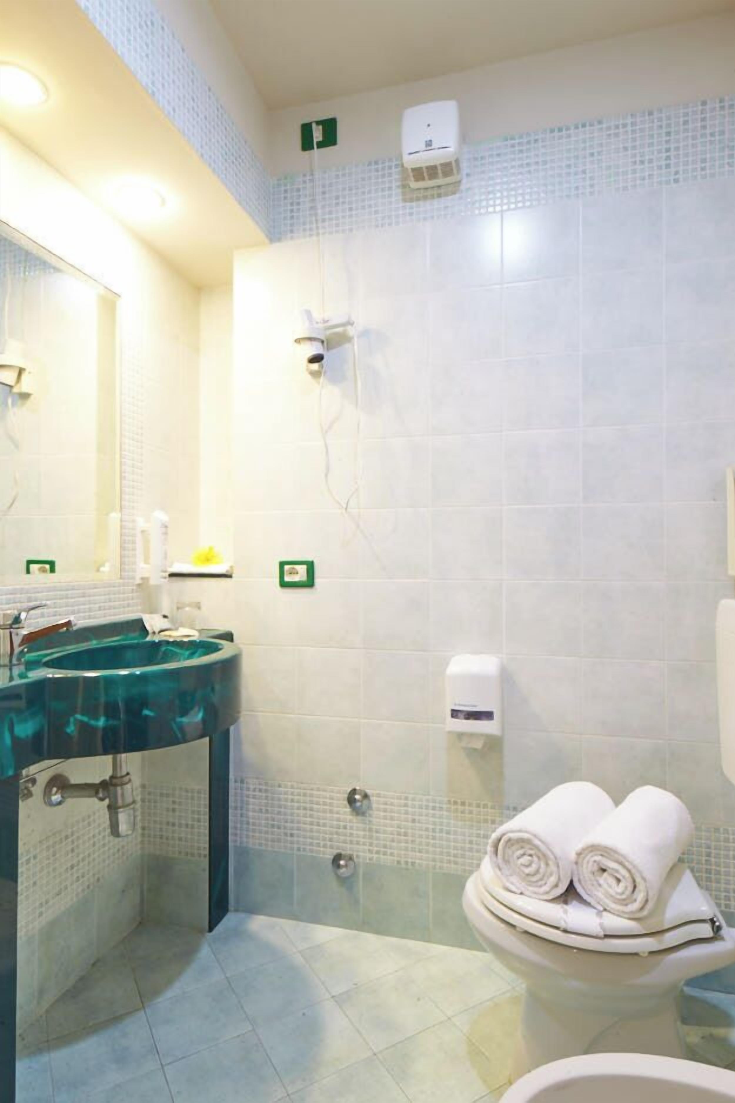 A bathroom with a glass-enclosed shower, a sink with a mirror, and a toilet with towels.