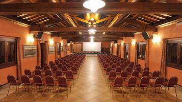 A conference room with rows of red chairs, wooden beams on the ceiling, and a projector screen at the front.