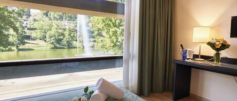 Habitación de hotel con cama, escritorio con lámpara y vista a una cascada y follaje.