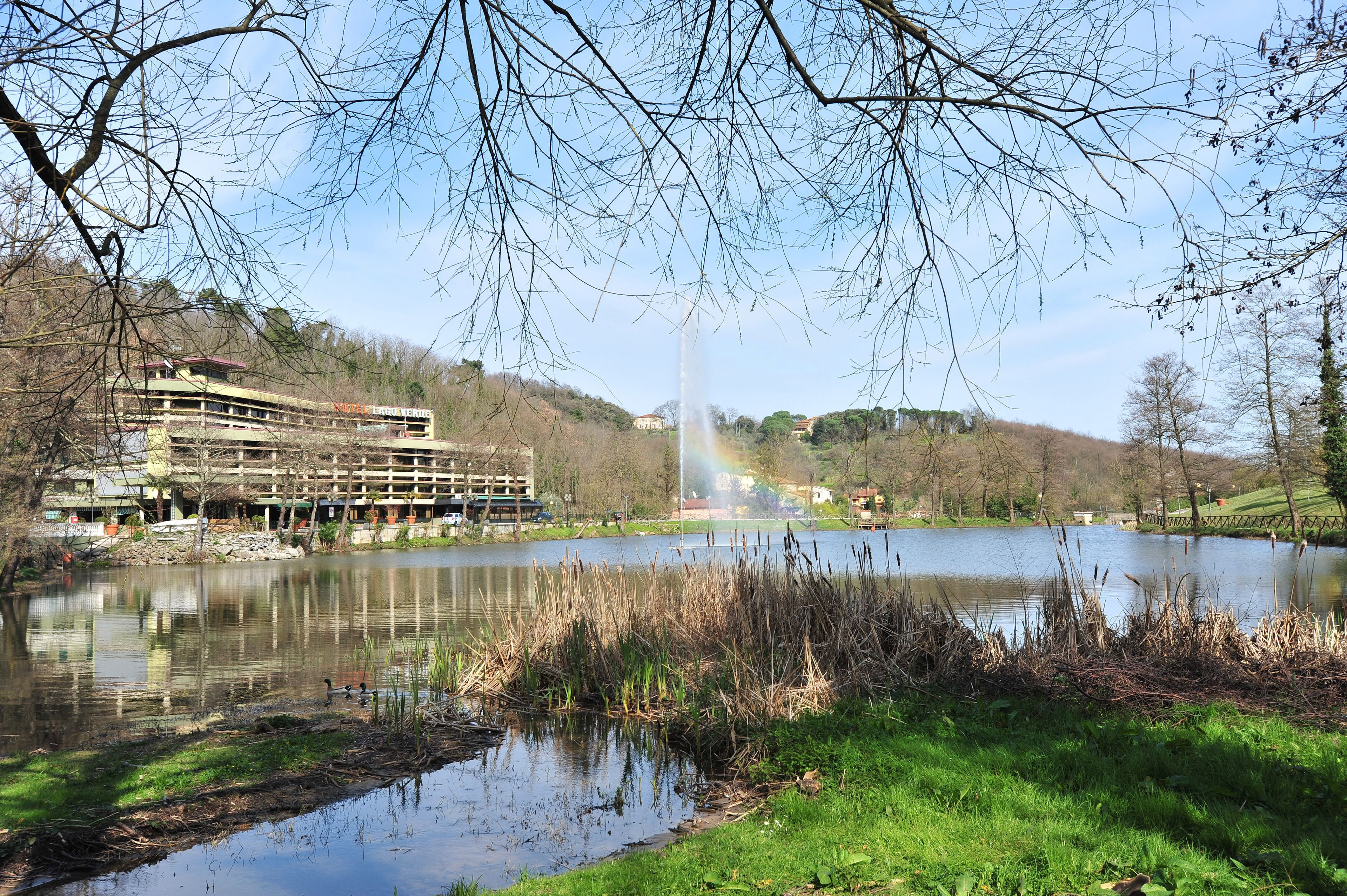 A lakeside view with a building, a fountain, and a reflection of the sky.