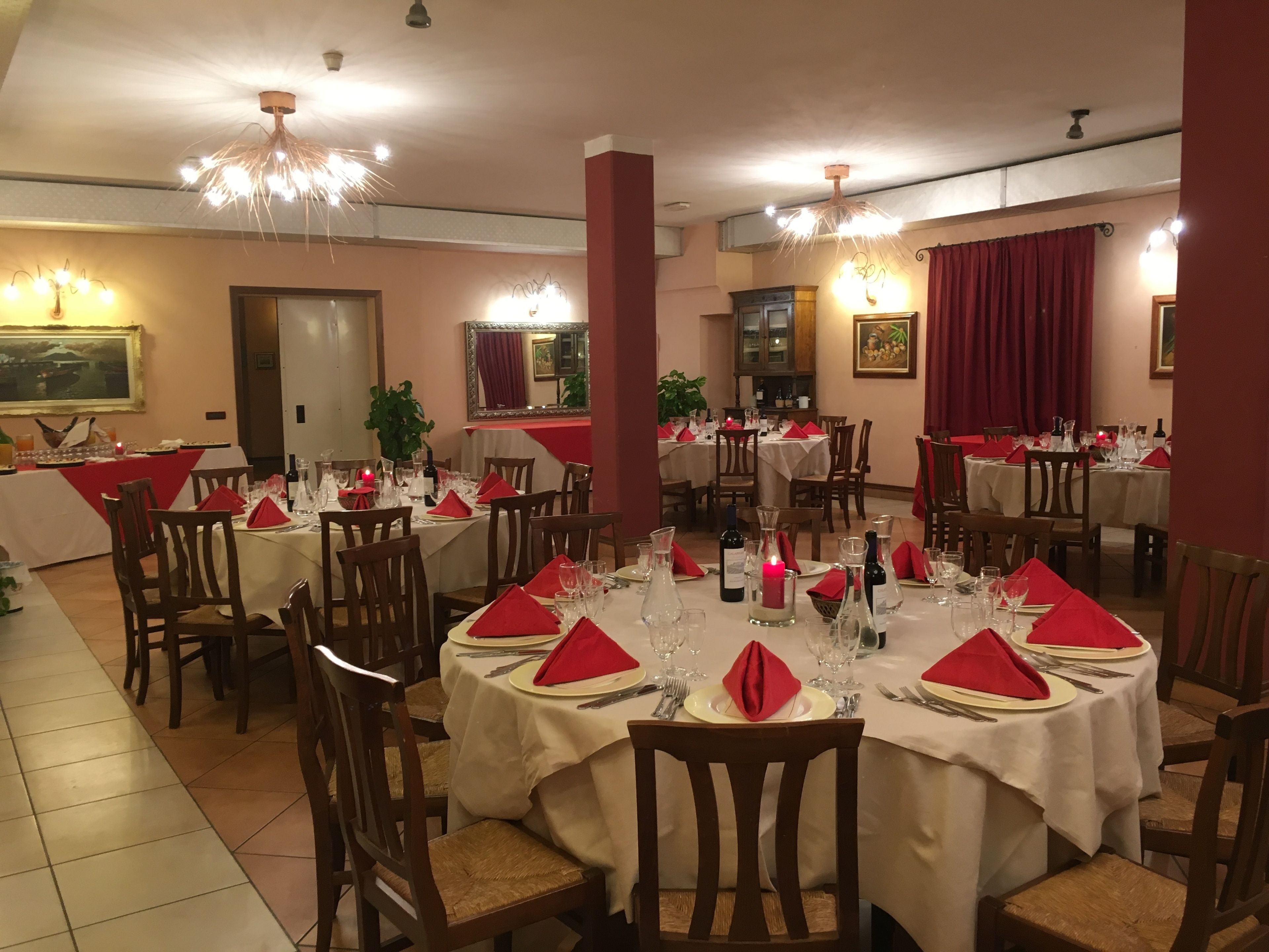 Un restaurante con mesas redondas, servilletas rojas y velas.