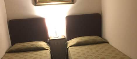 A small room with two single beds, a nightstand with a lamp, and a painting on the wall.