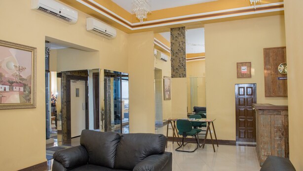 A lobby with a black leather sofa, a wooden cabinet, and a green chair. There are air conditioning units on the wall and a chandelier. - Villa Iguaçu Palace Hotel (Foz do Iguaçu)
