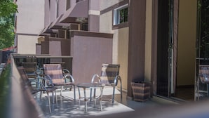 An outdoor seating area with wicker chairs and a glass table, adjacent to a building with a sliding glass door. - Villa Iguaçu Palace Hotel (Foz do Iguaçu)