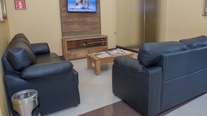 A modern living room with two black leather sofas, a wooden coffee table, and a flat-screen TV mounted on a wooden wall. - Villa Iguaçu Palace Hotel (Foz do Iguaçu)