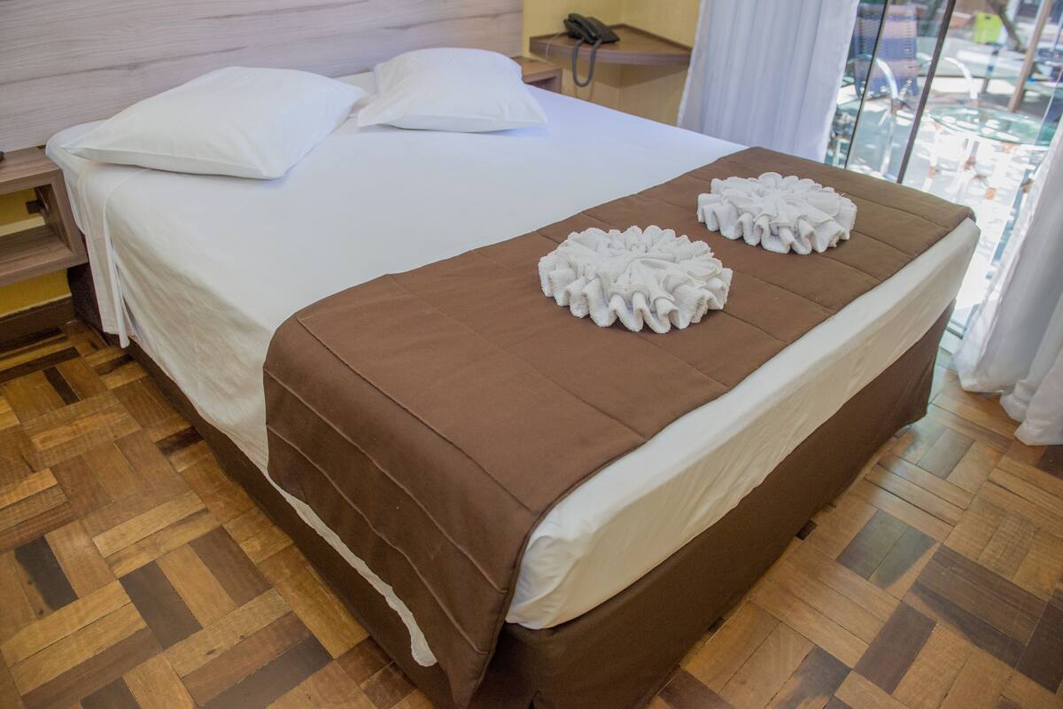 A neatly made bed with a brown bedspread and two white towels on the footboard.