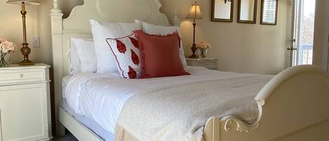 A bedroom with a white bed, two bedside tables with lamps, a marble-patterned floor, and a wooden ceiling.