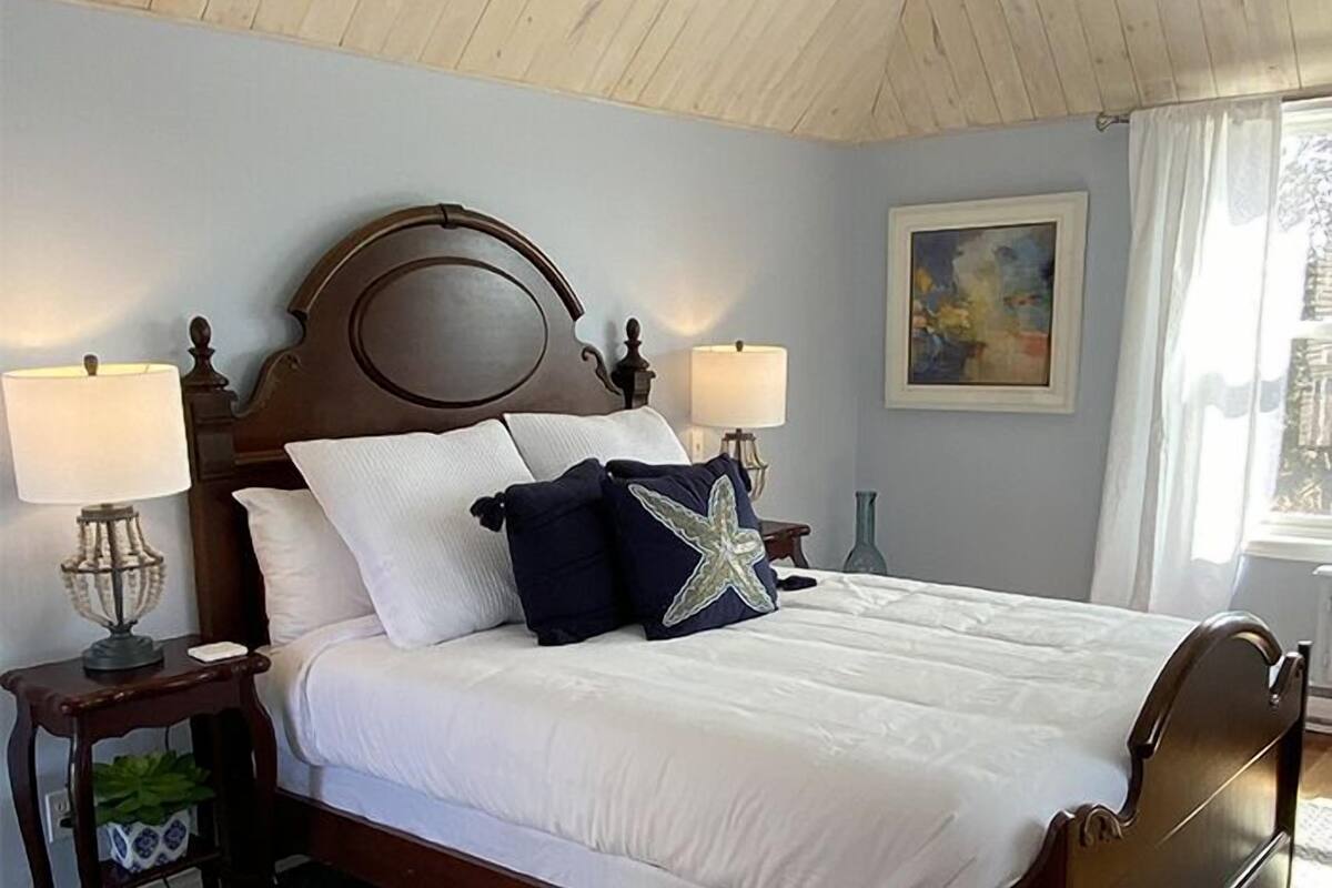 A neatly made bed with white linens and decorative pillows, including a star-shaped one, in a room with wooden ceiling and walls.