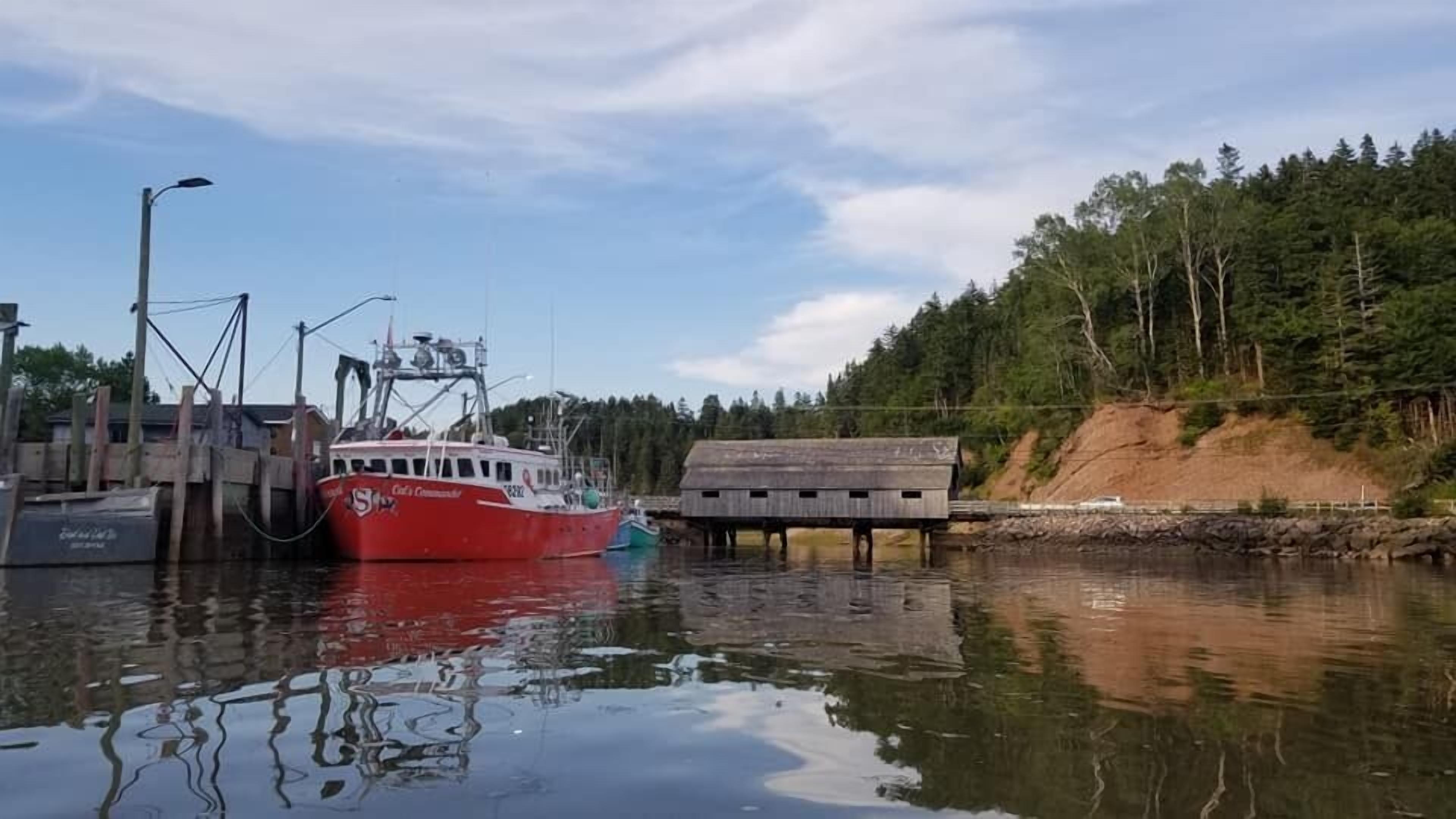A red boat docked at a pier with a wooden structure nearby.