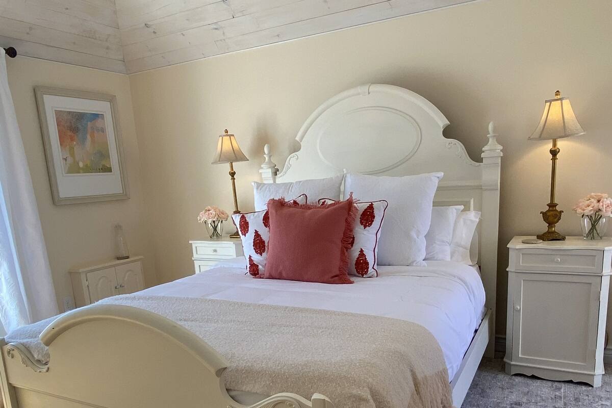 A neatly made bed with white bedding and a red pillow, flanked by two bedside tables with lamps.