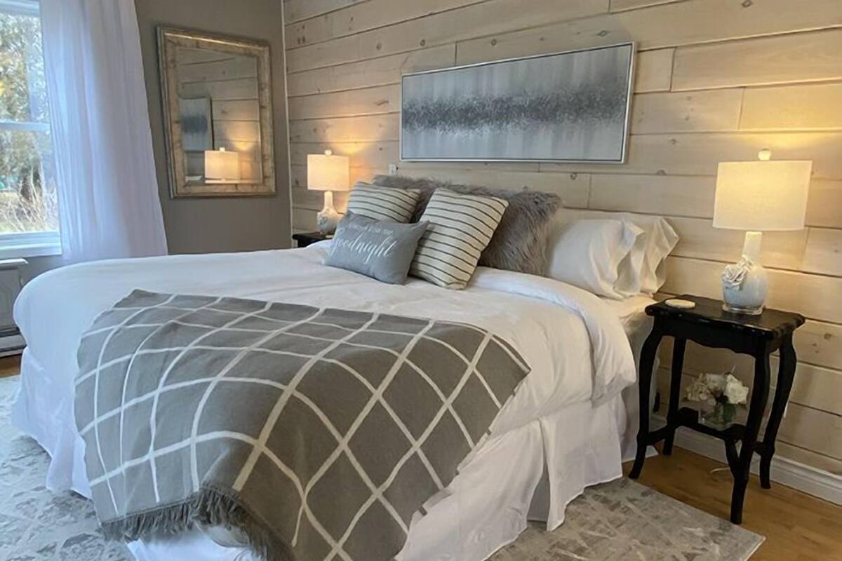 A bedroom with a large bed, two bedside tables with lamps, a mirror, and a painting on the wall.