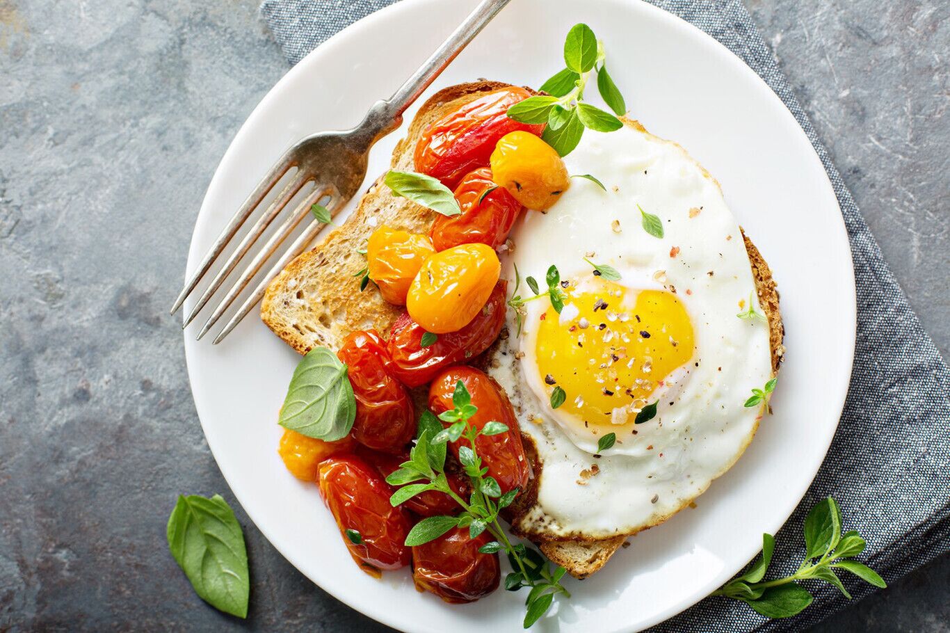 A plate with a fried egg, cherry tomatoes, and a piece of toast, garnished with herbs.