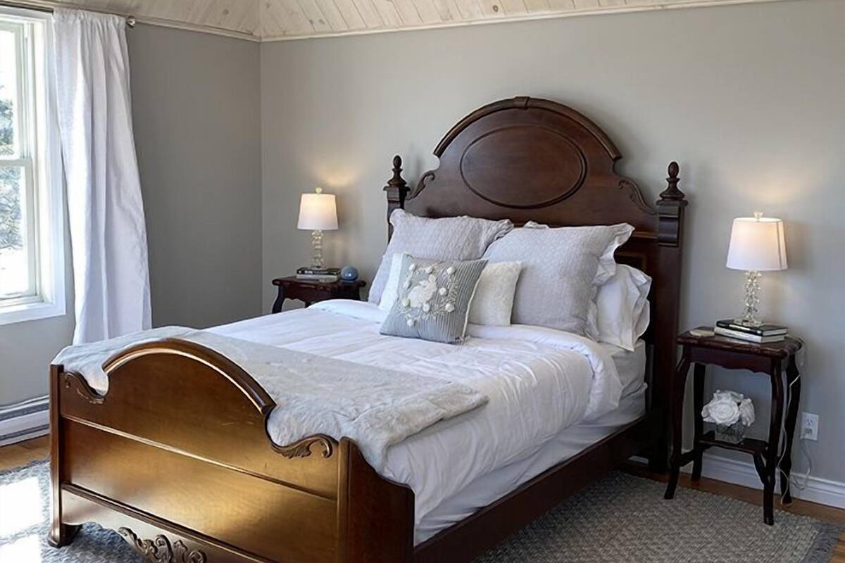 A bedroom with a wooden bed, two bedside tables with lamps, a window with curtains, and a rug on the floor.