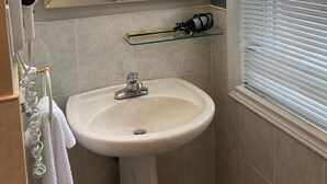 A bathroom with a white sink, a mirror above it, and a window with blinds.