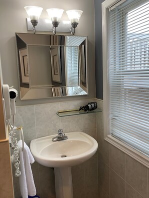 A bathroom with a white sink, a mirror above it, and a window with blinds.