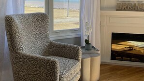 Una sala de estar con un sillón estampado, una mesita con una orquídea en maceta y una chimenea con un letrero que dice 'DREAM'.