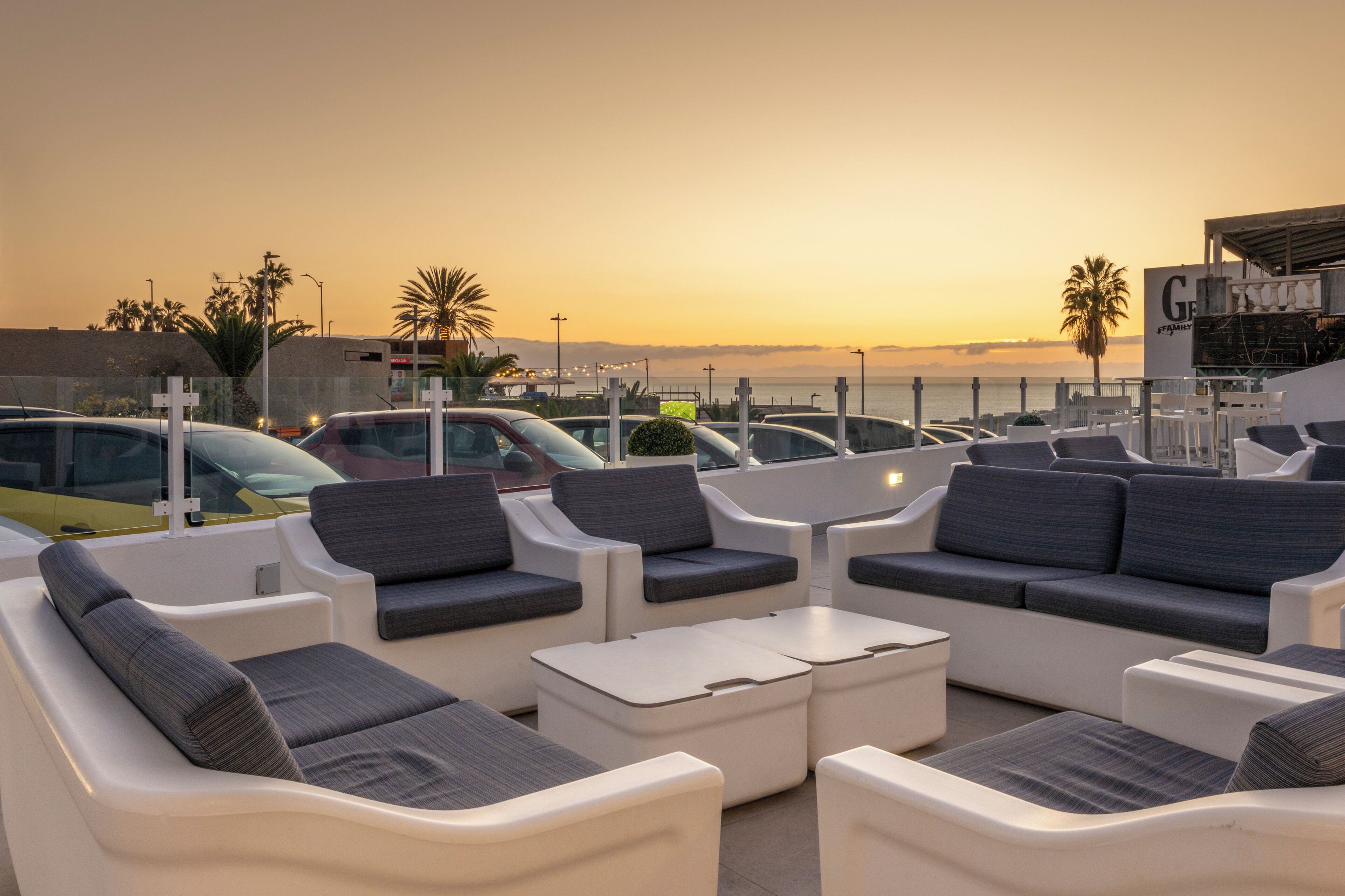 Outdoor seating with a view of the sunset and parked cars.