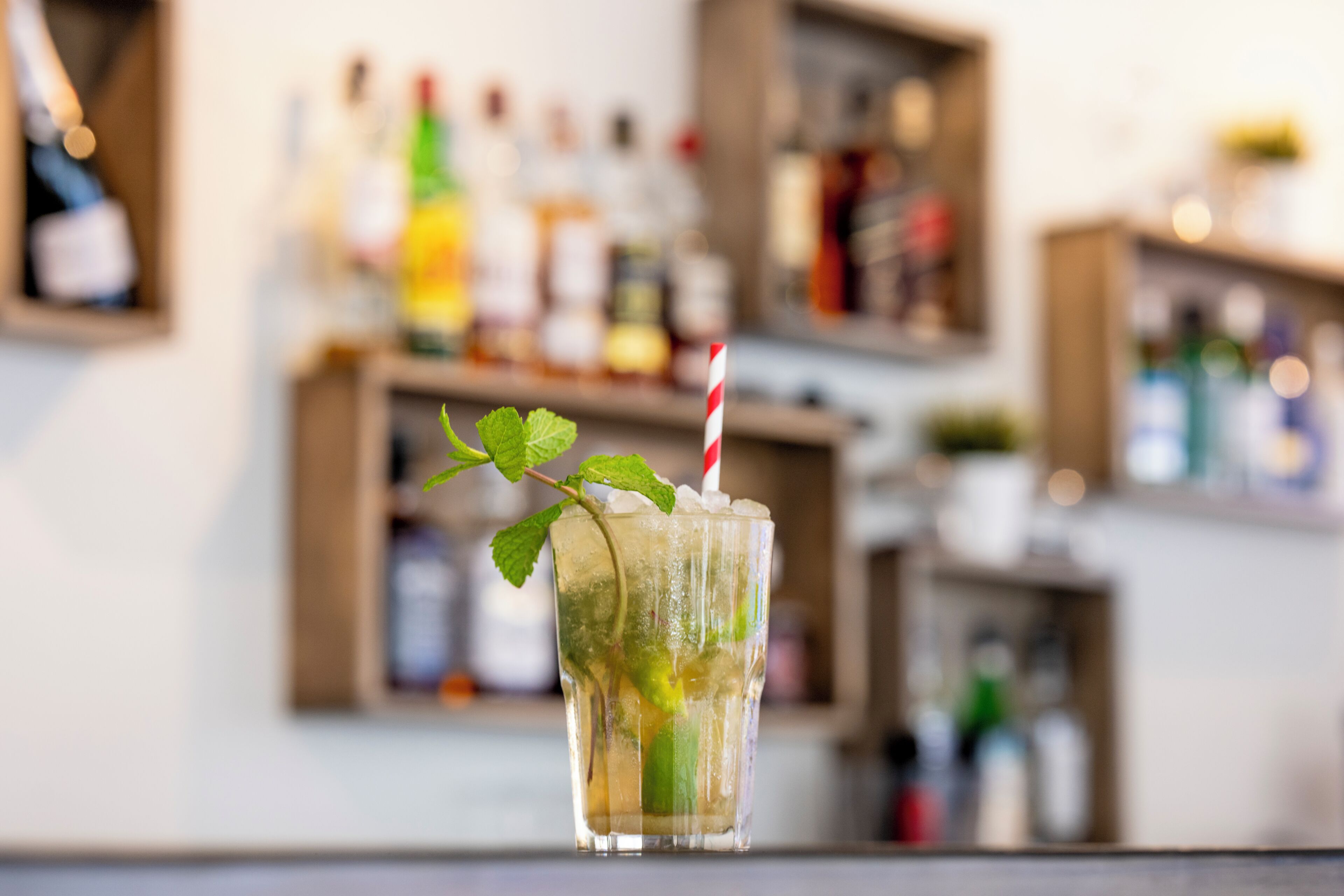 A bar setting with a glass of drink, ice, mint, and a straw.
