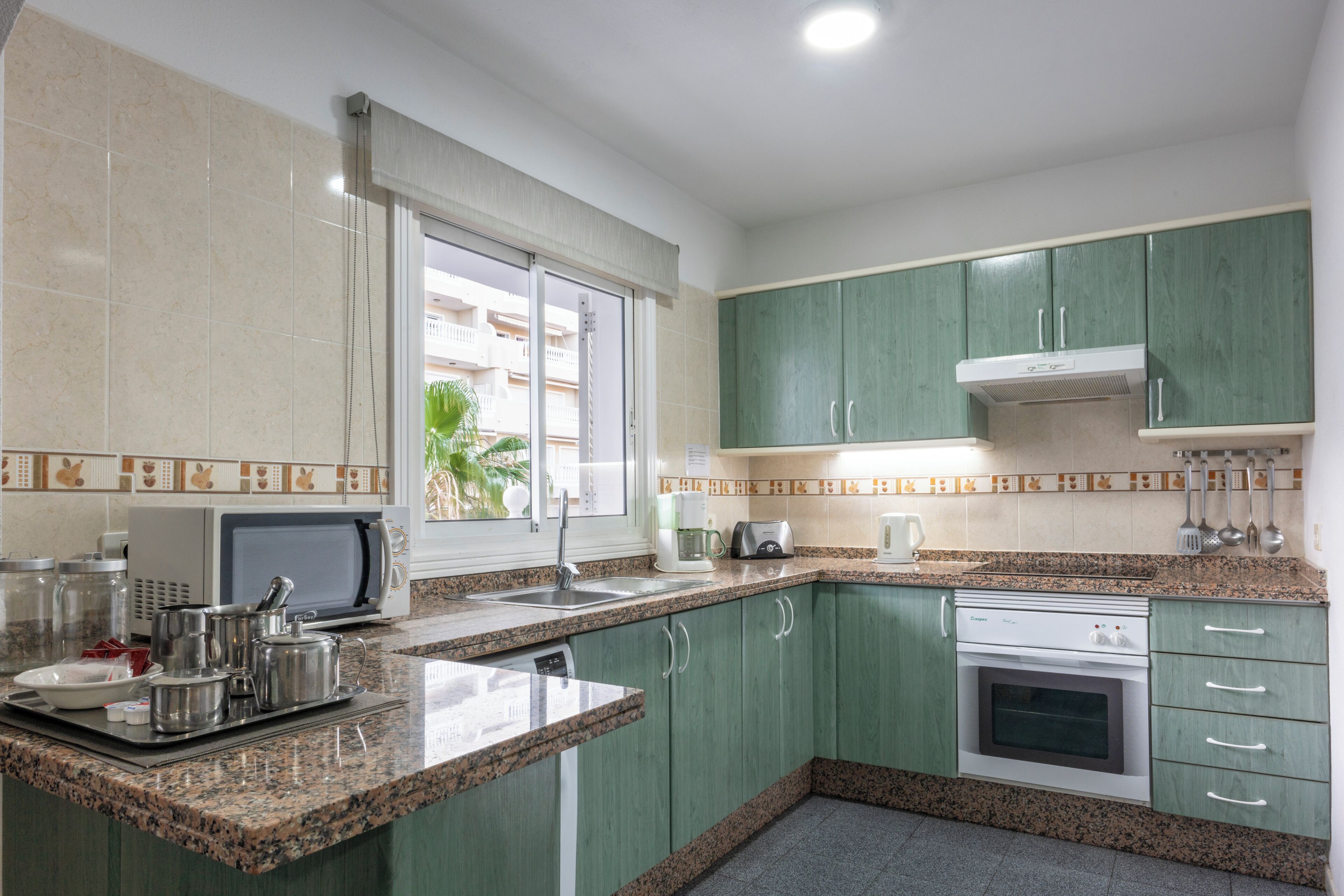 A kitchen with green cabinets, a microwave, a toaster, and a stove.