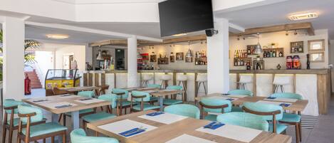 A restaurant with multiple tables and chairs, a bar area, and a television mounted on the wall.