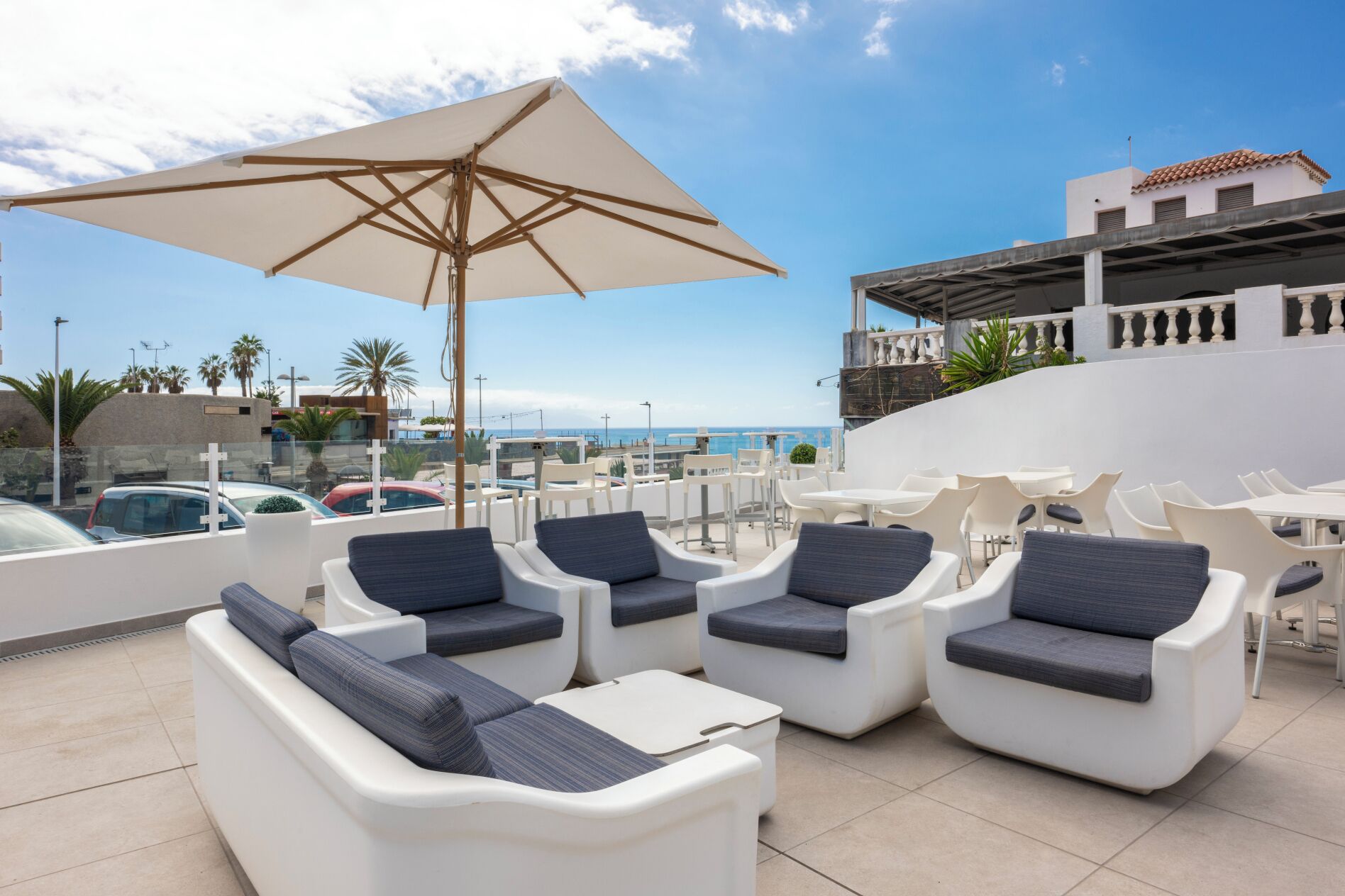 Una terraza en la azotea con mobiliario exterior blanco, un paraguas grande y vistas al mar.