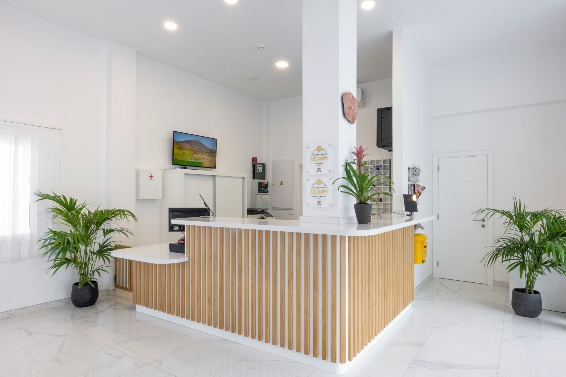 Un comptoir d'accueil avec un design composé de lattes de bois, un téléviseur à écran plat fixé au-dessus, et une horloge murale.