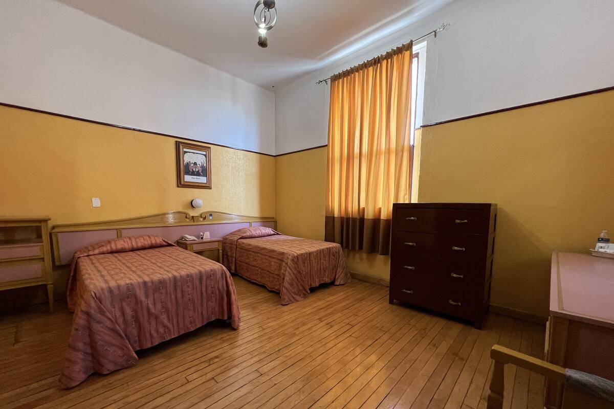 Habitación de hotel con dos camas, un escritorio, una cómoda y una ventana con cortinas.