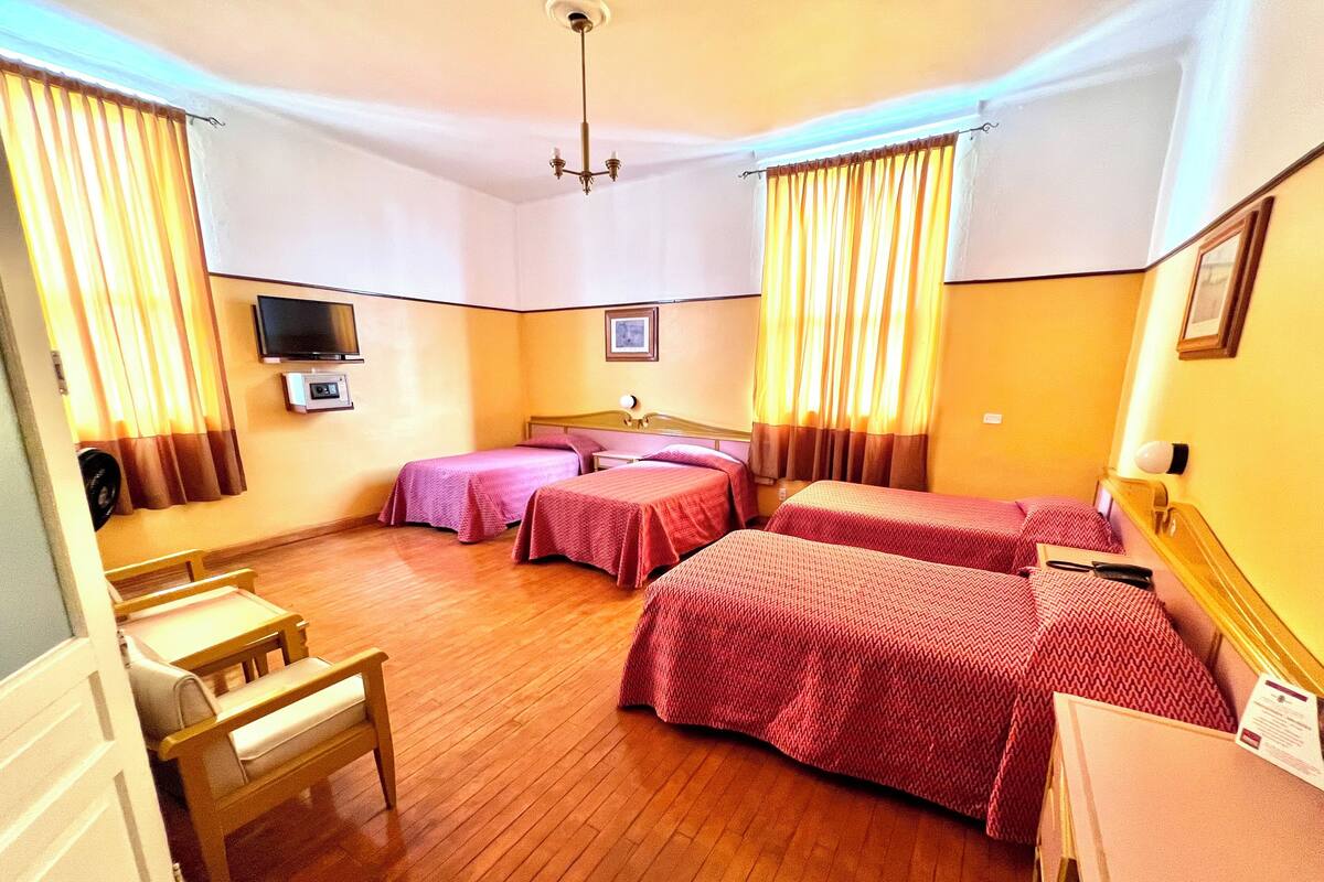 Una habitación de hotel con cuatro camas, televisión, escritorio y una silla.