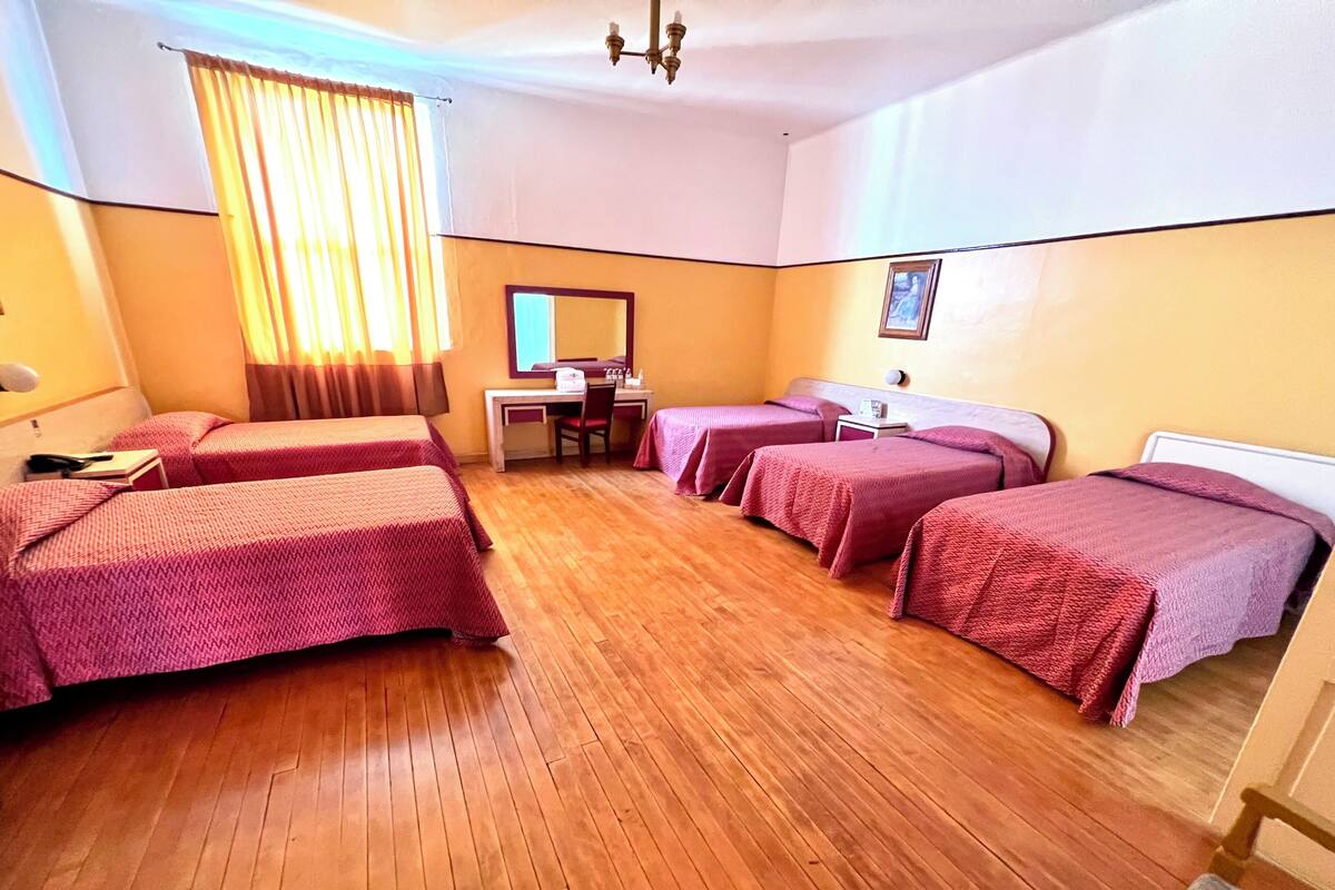 Habitación de hotel con cuatro camas, un escritorio, una silla, un espejo y piso de madera.